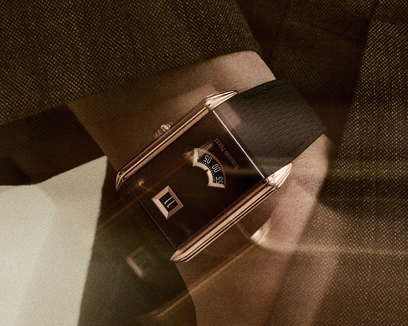 Rectangular wristwatch with a black dial, rose gold case, and black leather strap worn on a wrist.