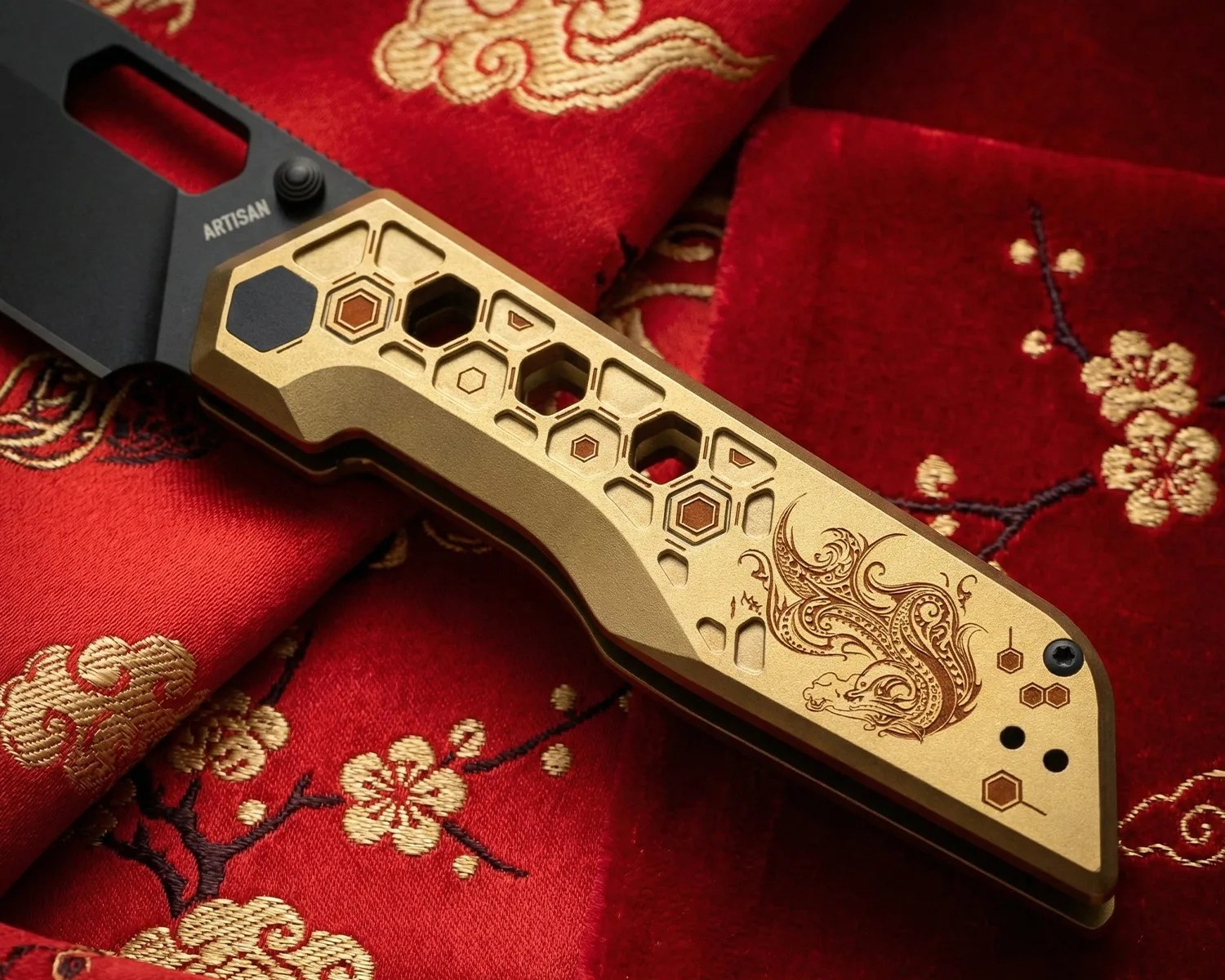 Close-up of a gold-toned knife handle with hexagonal cutouts and intricate dragon engraving, resting on red fabric with gold floral embroidery.