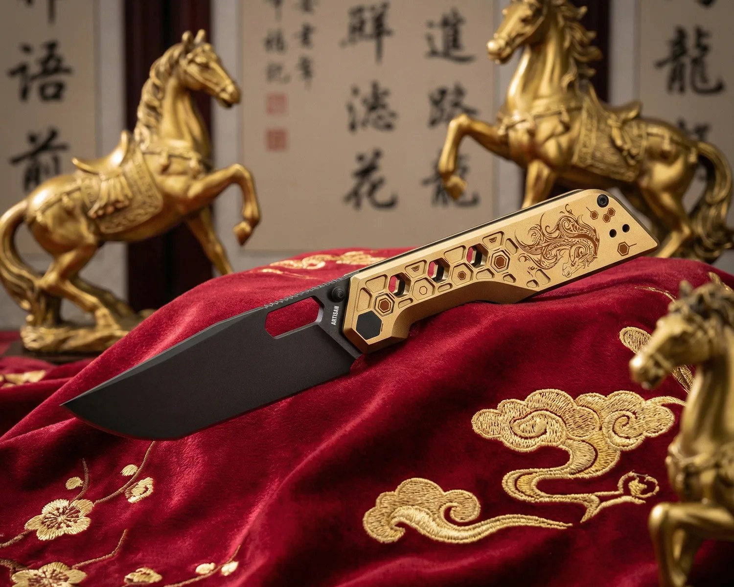 Black blade folding knife with gold handle featuring hexagonal cutouts and intricate dragon engraving on red embroidered fabric.