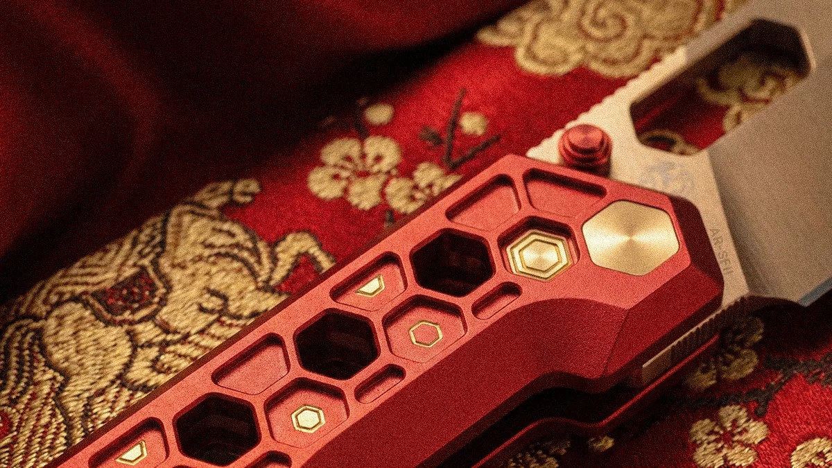 Close-up of a red and gold hexagonal-patterned knife handle resting on a red fabric with gold embroidery.
