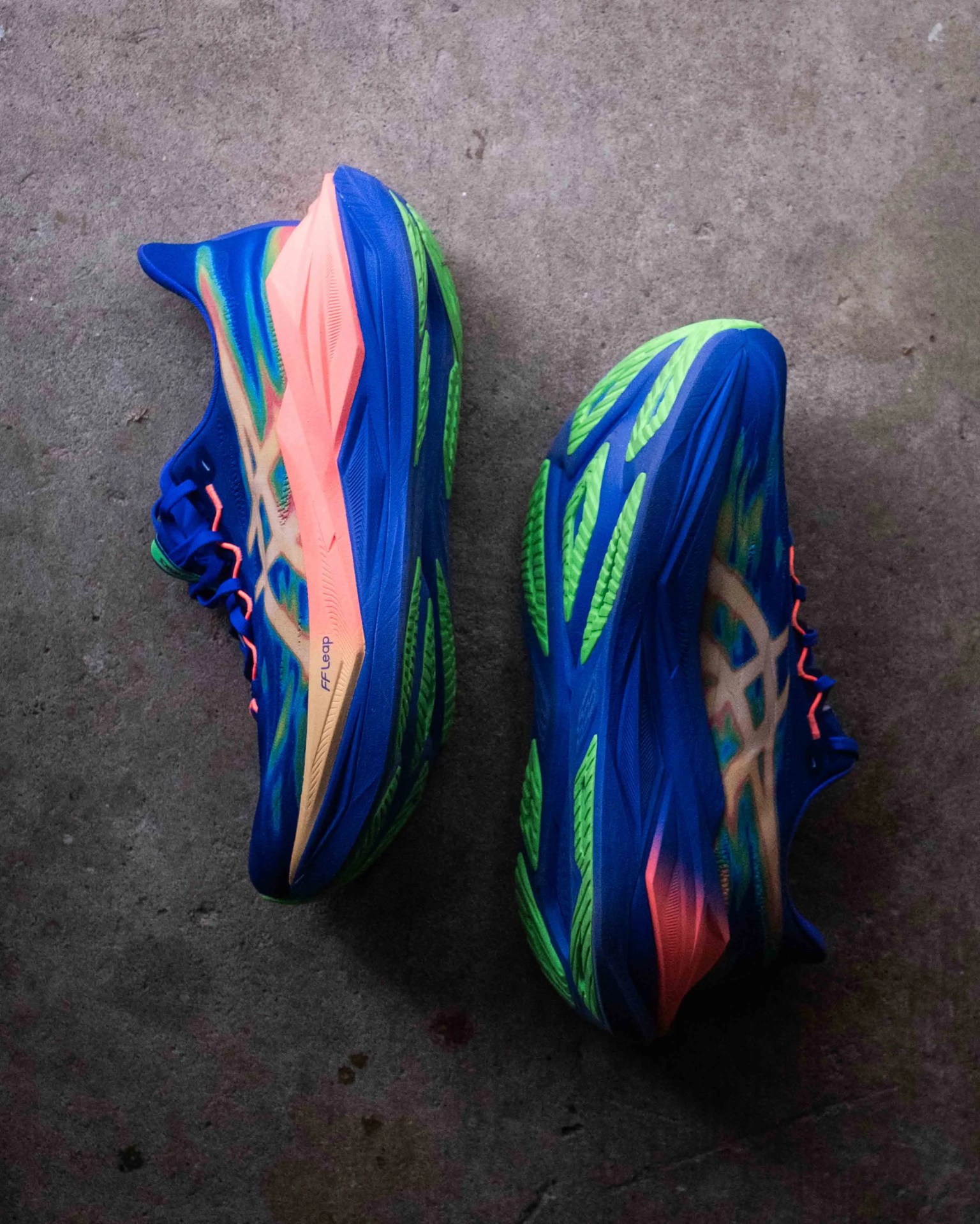 Pair of blue running shoes with green soles and pink accents on a concrete floor.