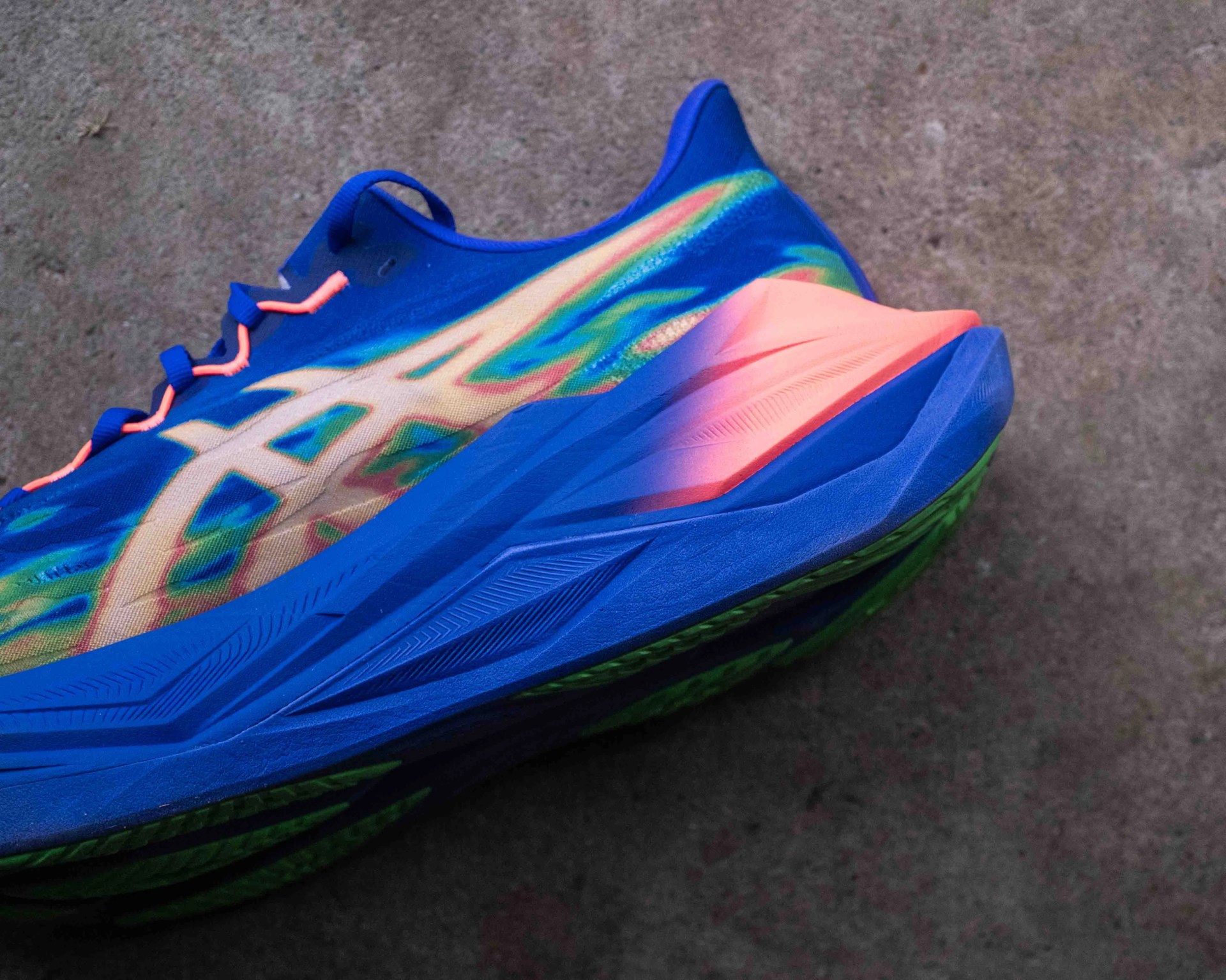 Blue running shoe with neon orange heel and green sole on a concrete surface.