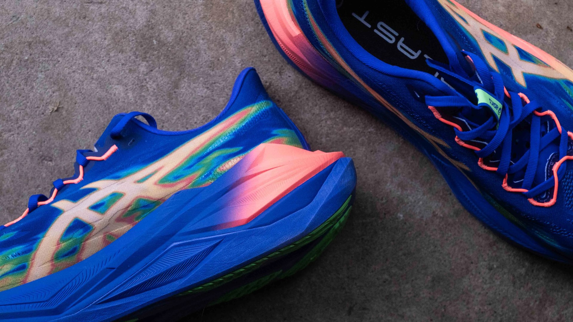 Pair of blue and neon orange running shoes with green accents on a concrete floor.