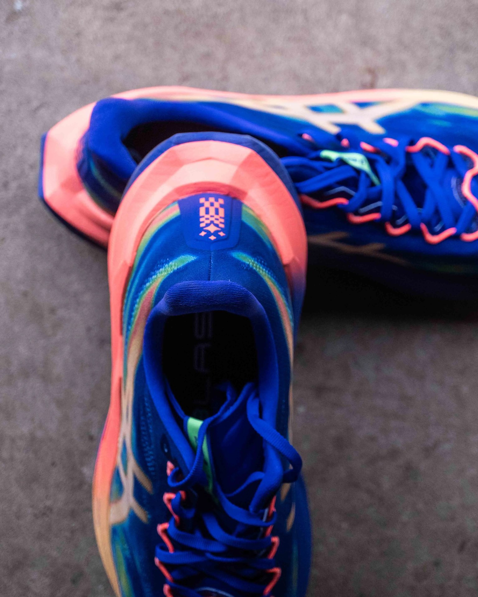Pair of blue and neon orange running shoes with blue laces on a gray surface.