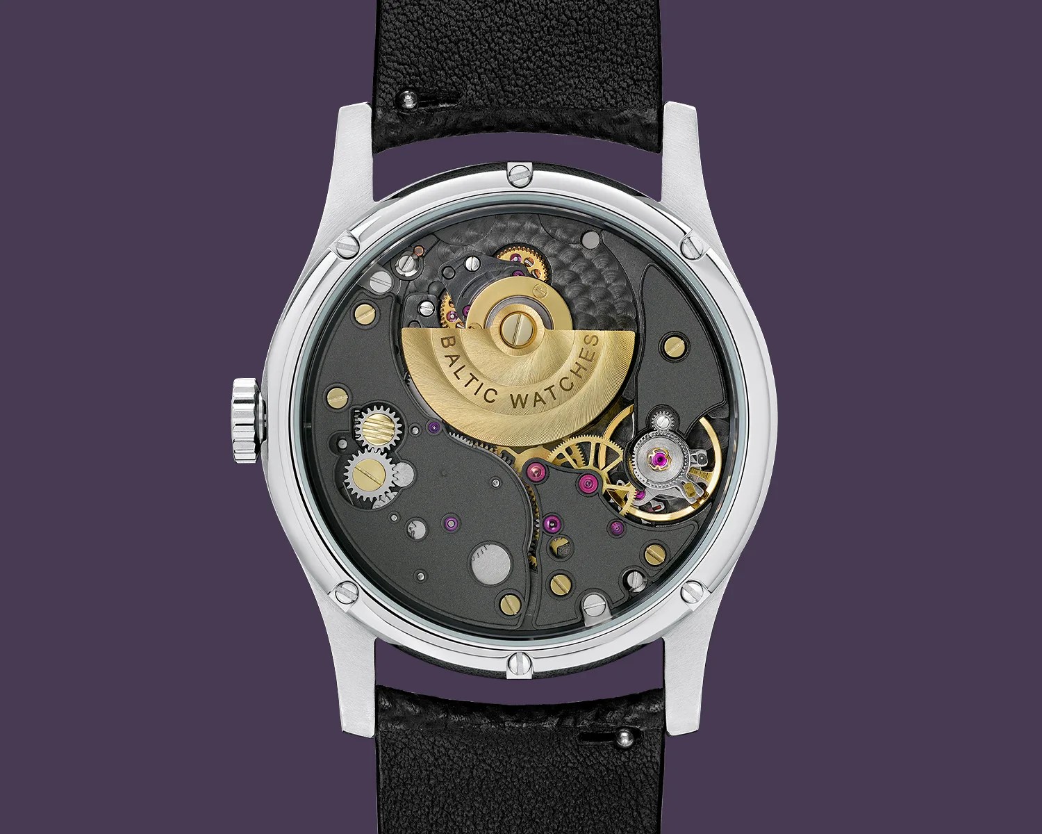 Close-up of a mechanical watch movement with visible gears and a gold rotor engraved "BALTIC WATCHES" inside a silver case with a black leather strap.