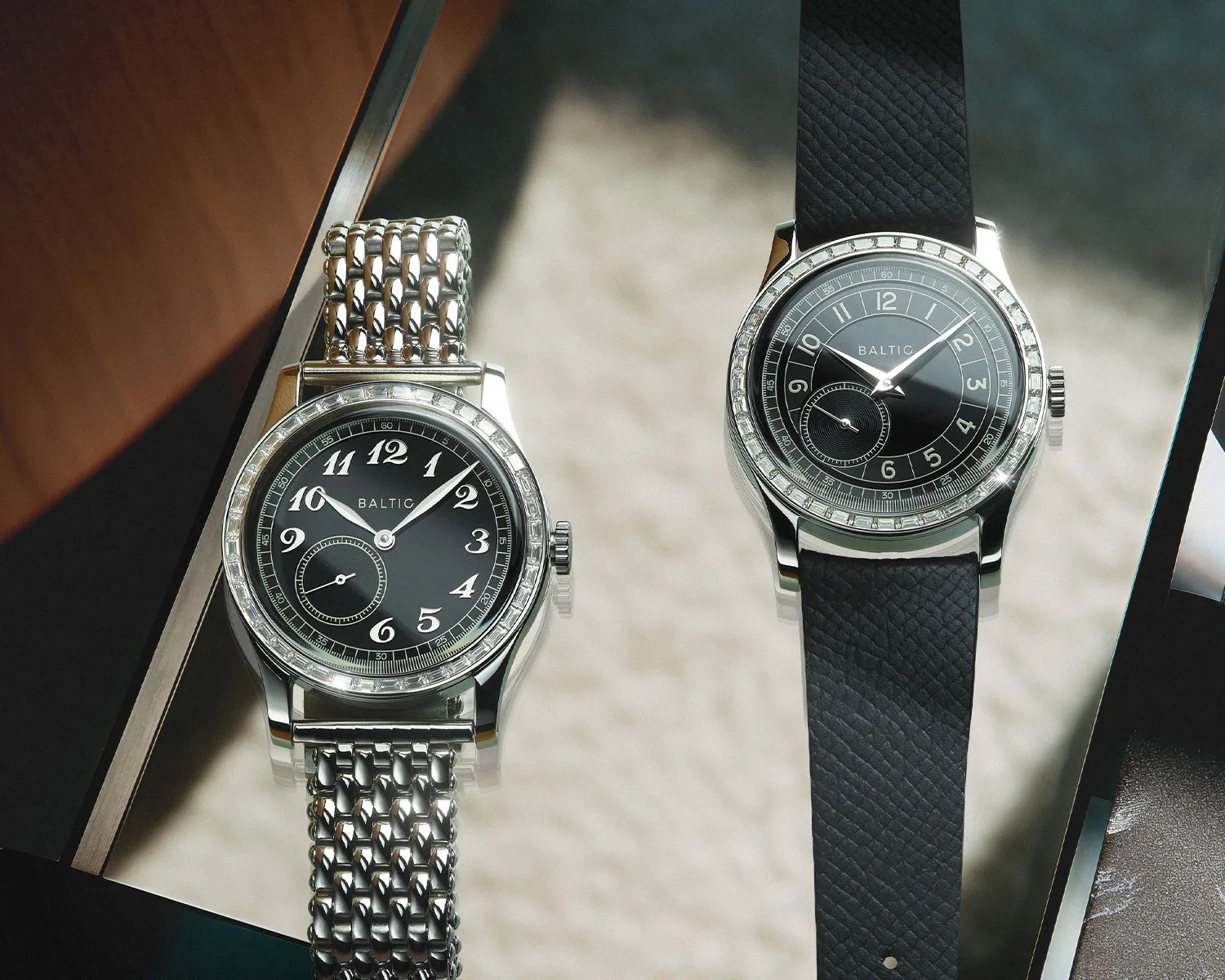 Two Baltic wristwatches with black dials and moissanite bezels, one with a silver metal bracelet and the other with a black leather strap.