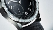 Close-up of a black watch face with silver numerals and a moissanite-studded bezel on a textured black leather strap.