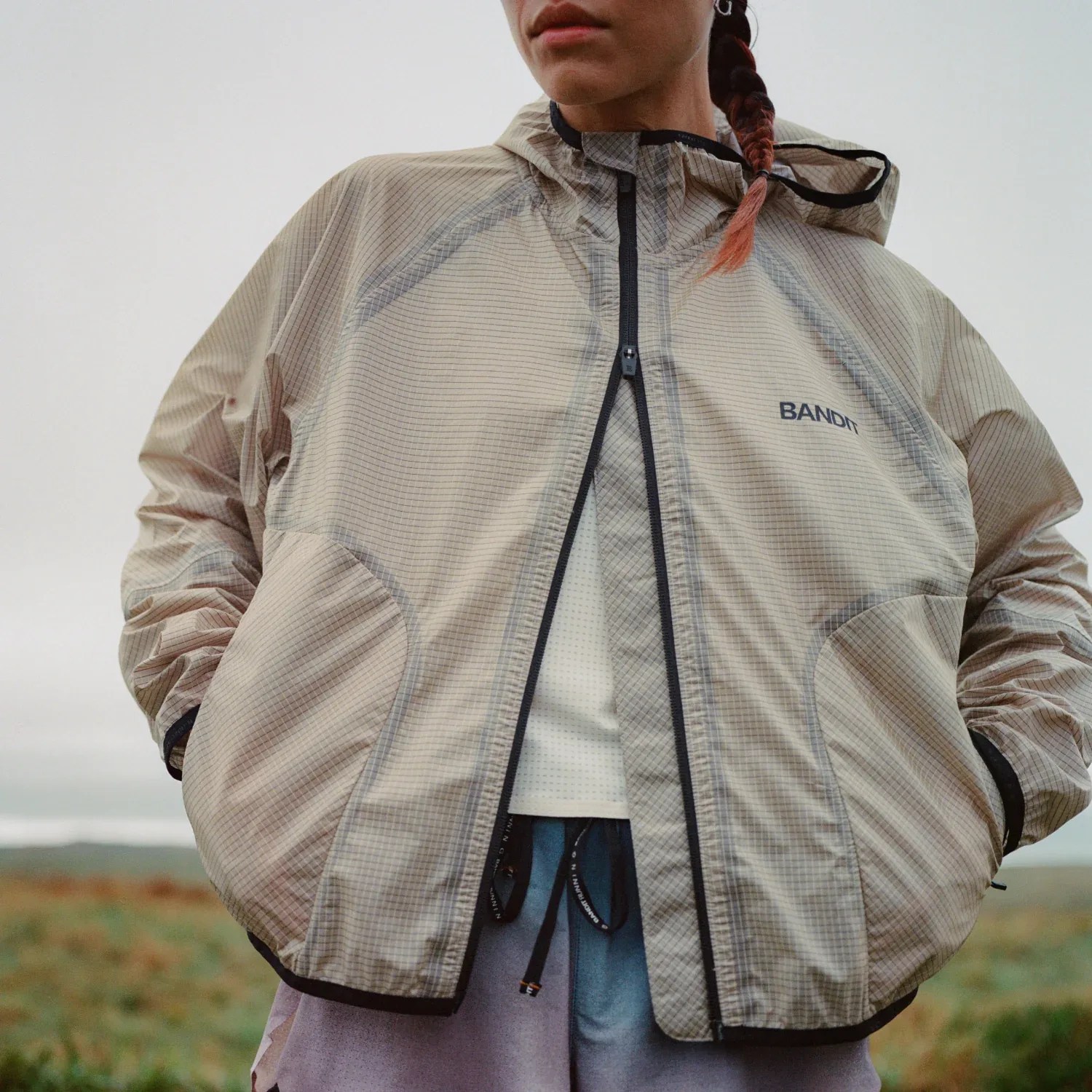 Light beige hooded jacket with black zipper and "BANDIT" logo on the chest, worn over a white top.