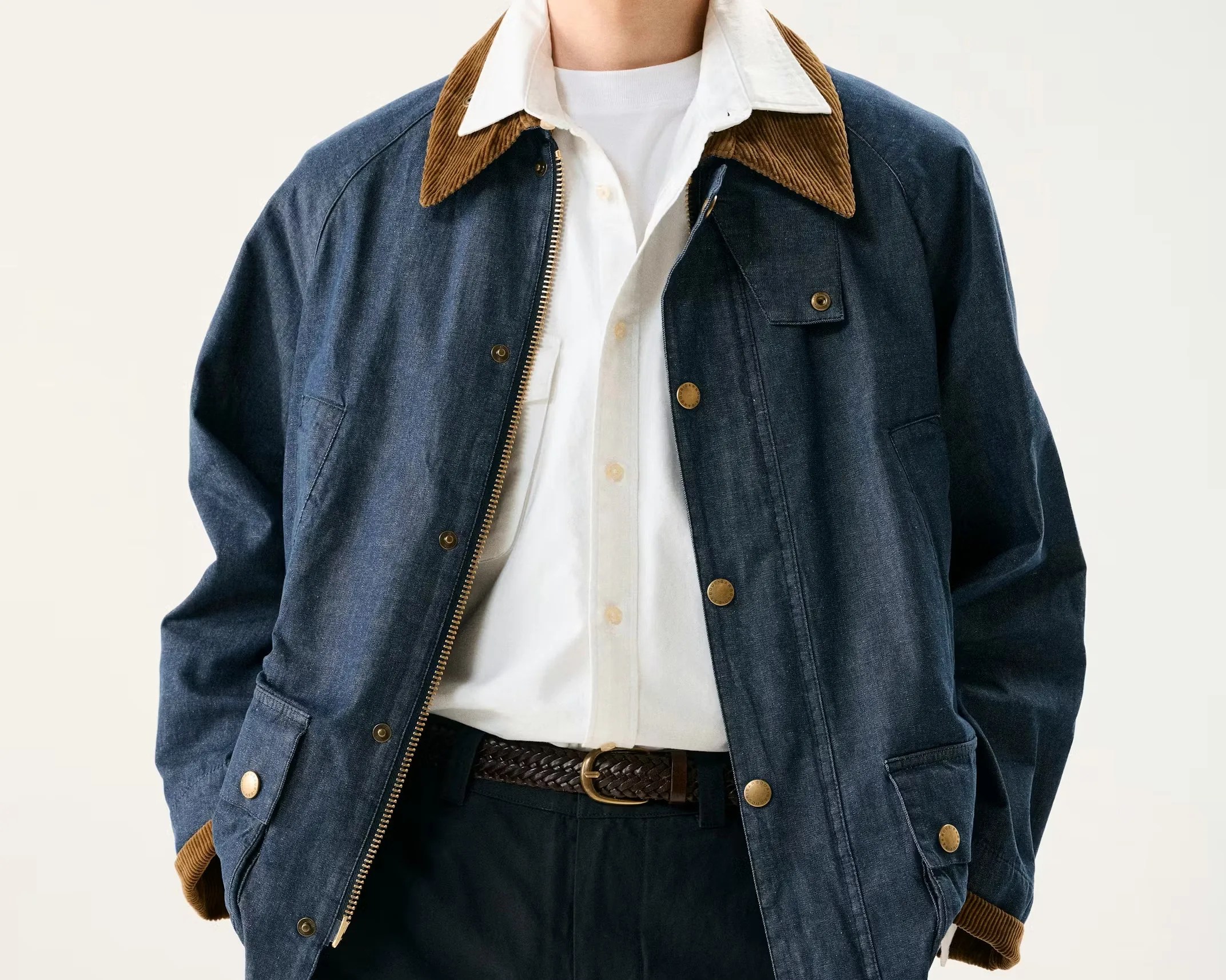 Denim jacket with brown corduroy collar and cuffs worn over a white button-up shirt and black pants with a braided brown belt.