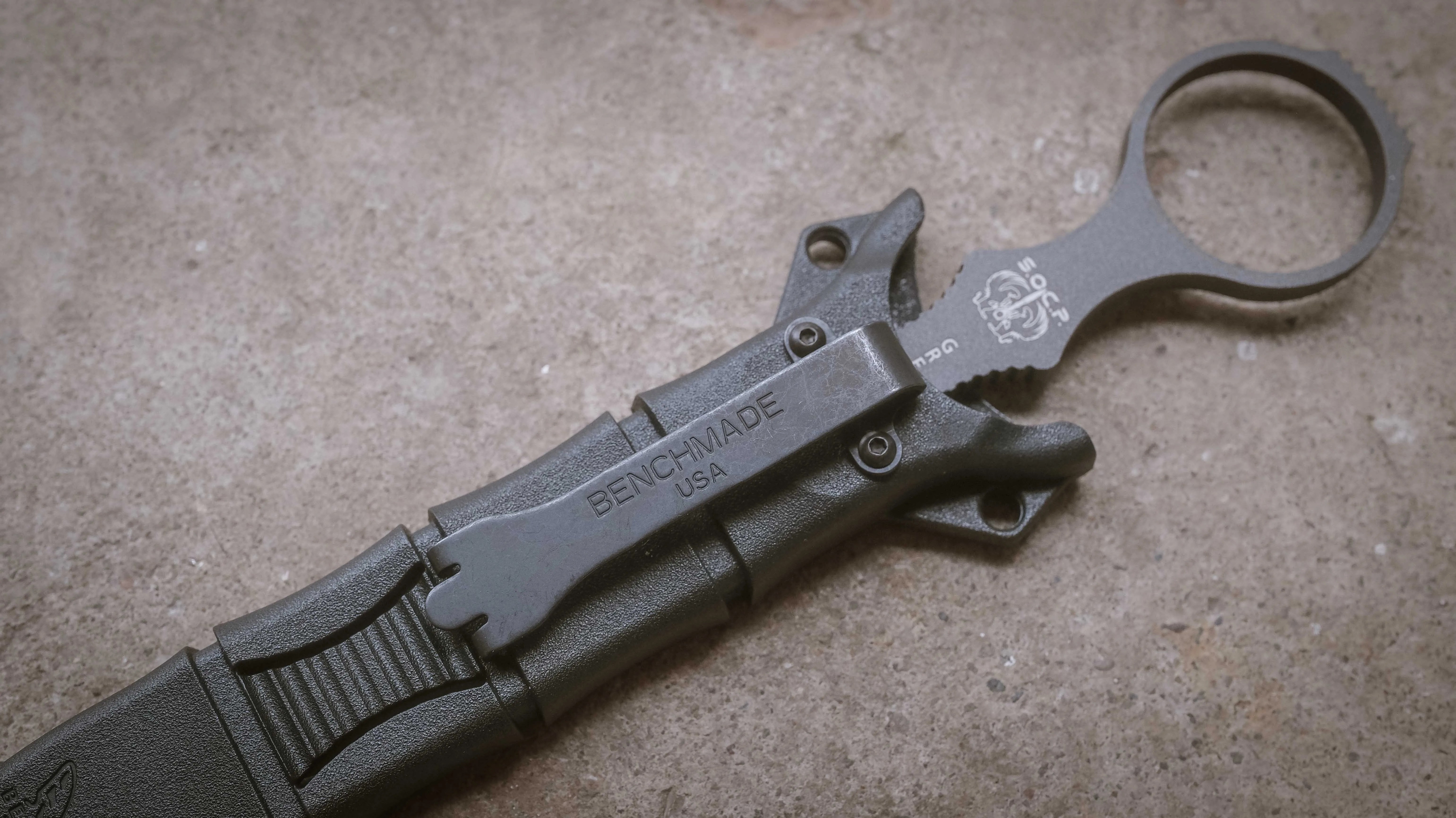 Black Benchmade knife sheath with belt clip and finger ring on a concrete surface.