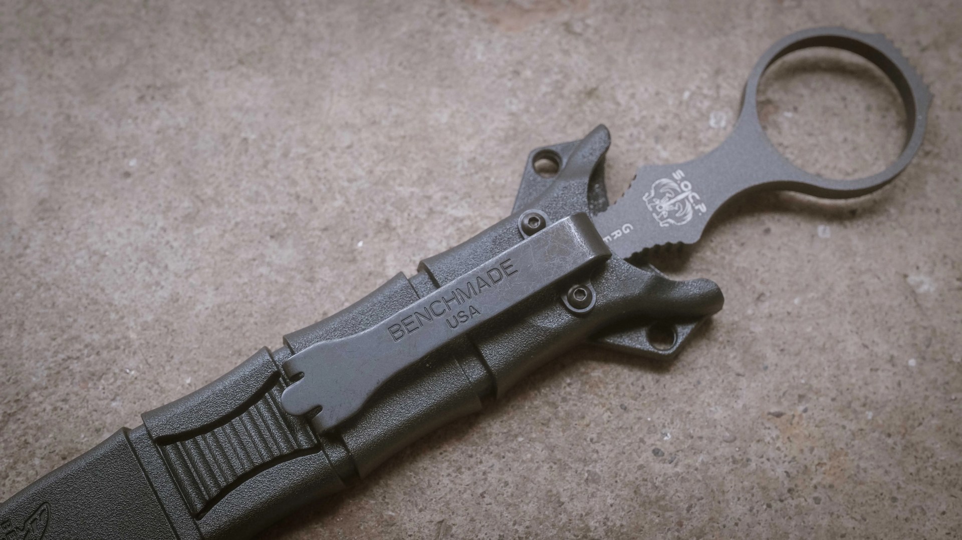 Black Benchmade knife sheath with belt clip and finger ring on a concrete surface.