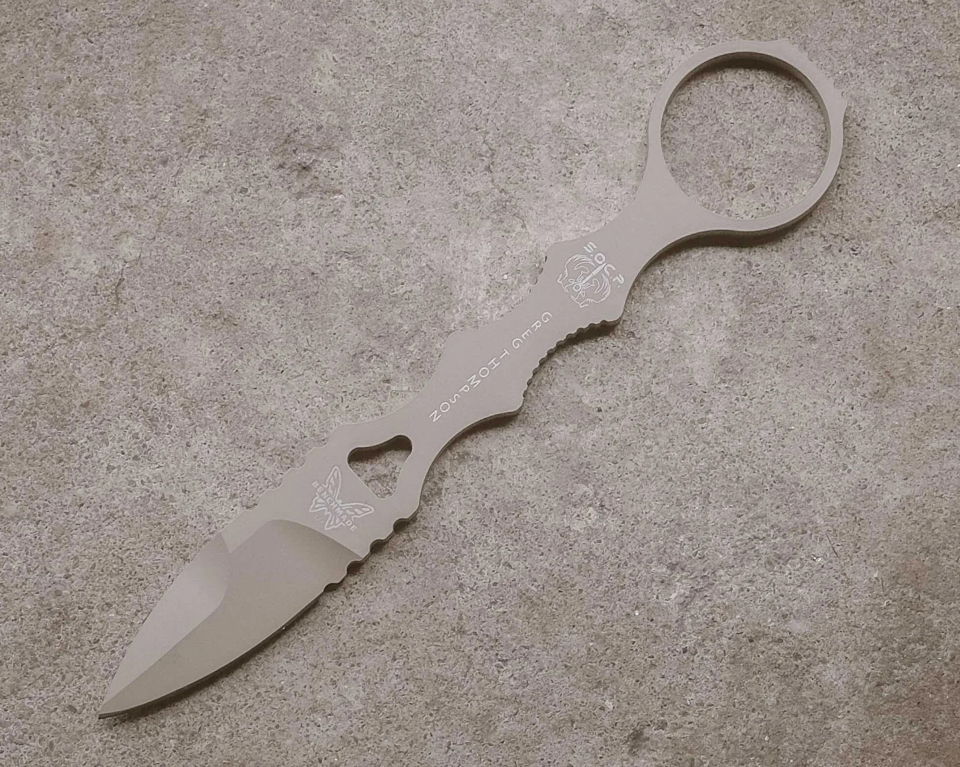 Small tactical knife with a finger ring and a matte gray finish on a rough concrete surface.