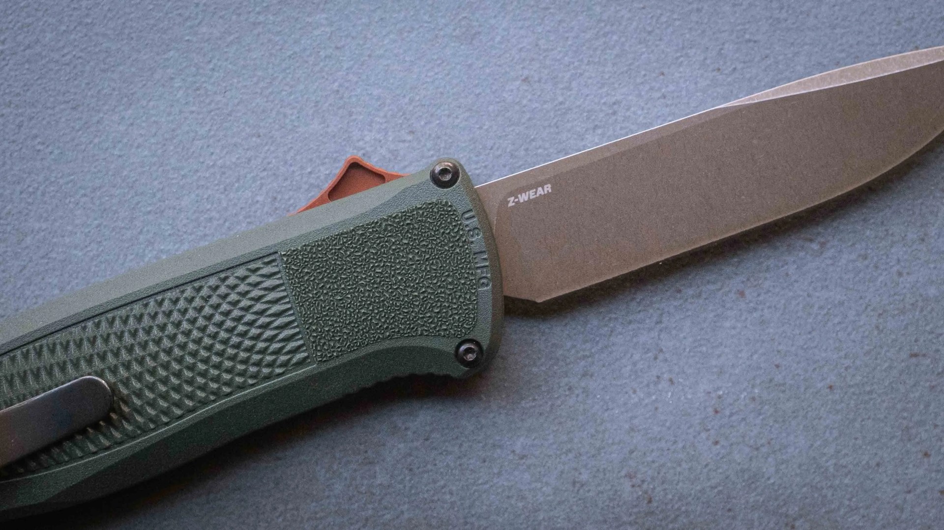 Folding knife with textured green handle and stonewashed blade marked "Z-WEAR" on a gray surface.