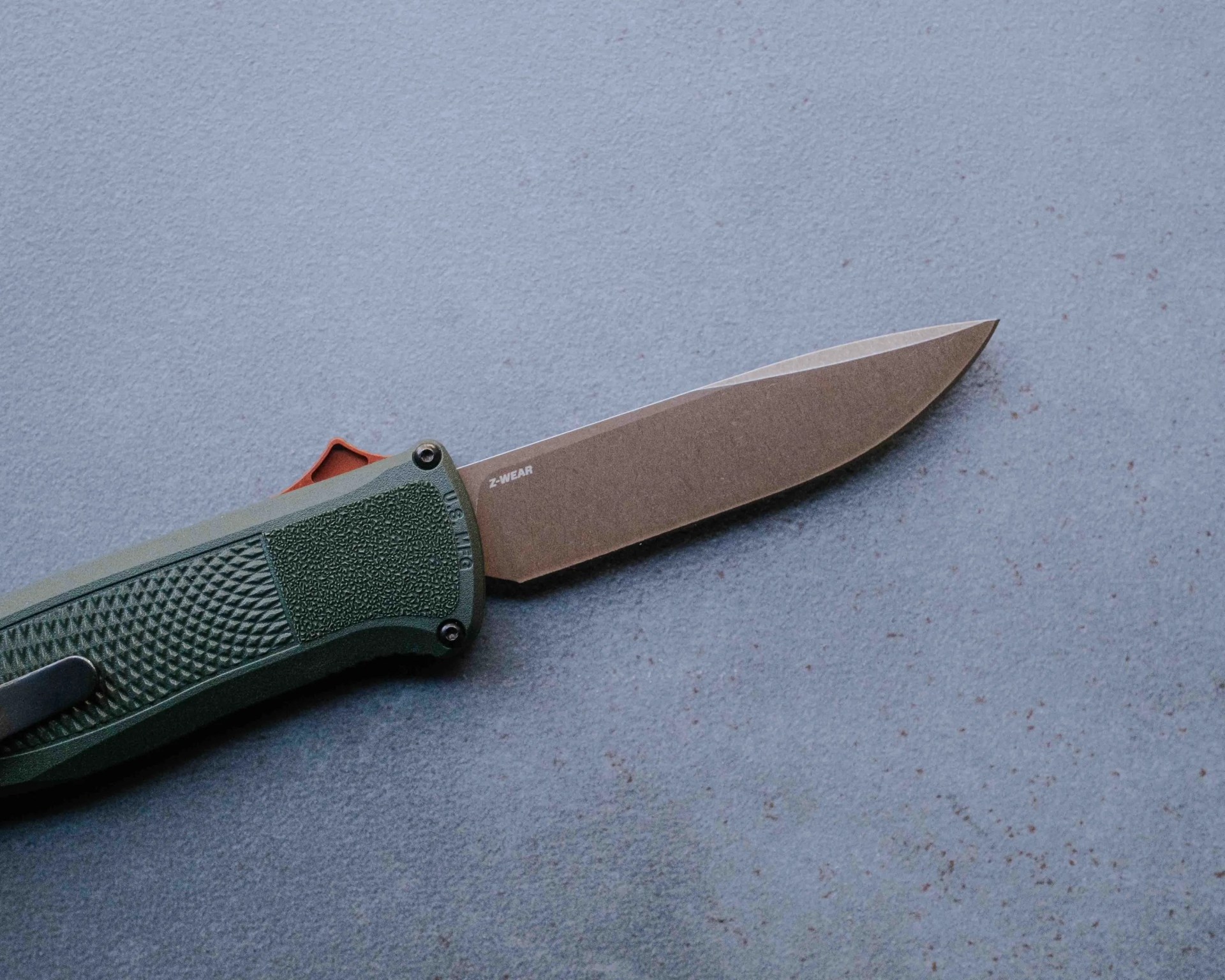 Folding knife with textured green handle and stonewashed blade marked "Z-WEAR" on a blue surface.