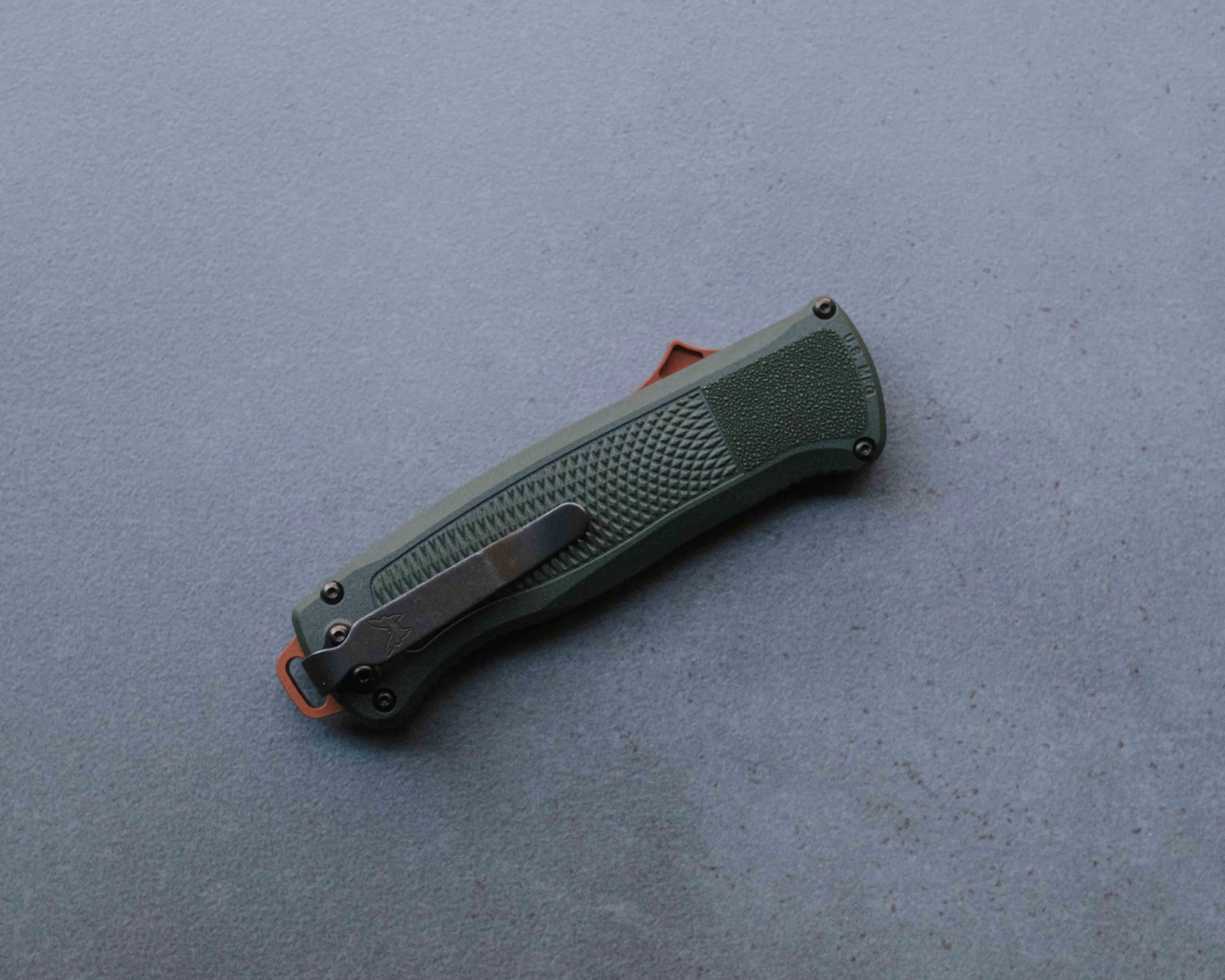 Green textured folding knife with black clip and orange accents on a gray surface.