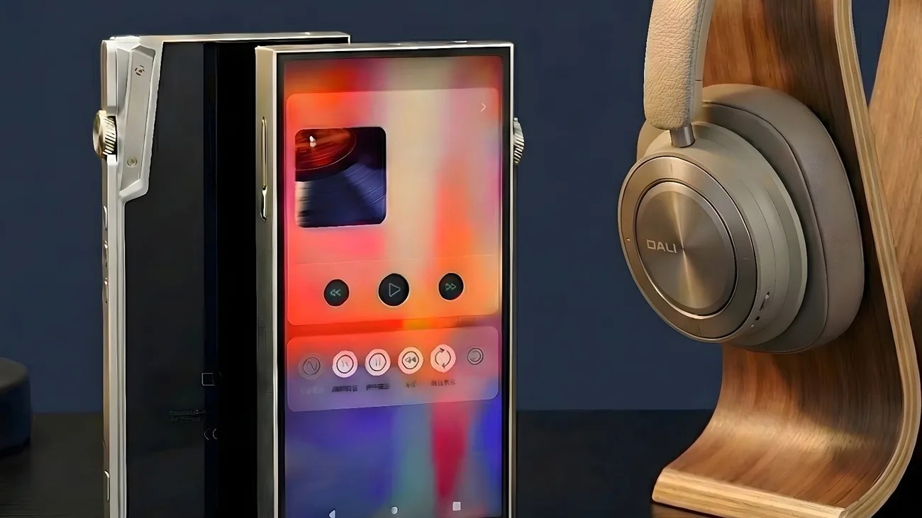 Silver and black digital music player with a colorful screen next to beige DALI headphones on a wooden stand.