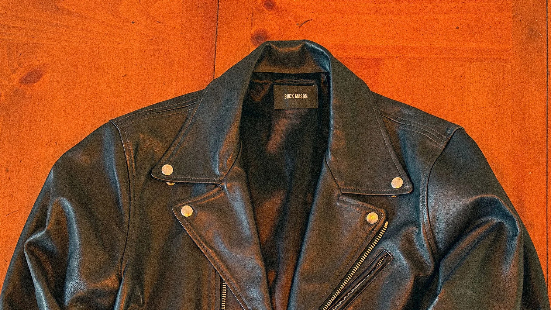 Black leather biker jacket with silver snap buttons and zipper on a wooden surface.