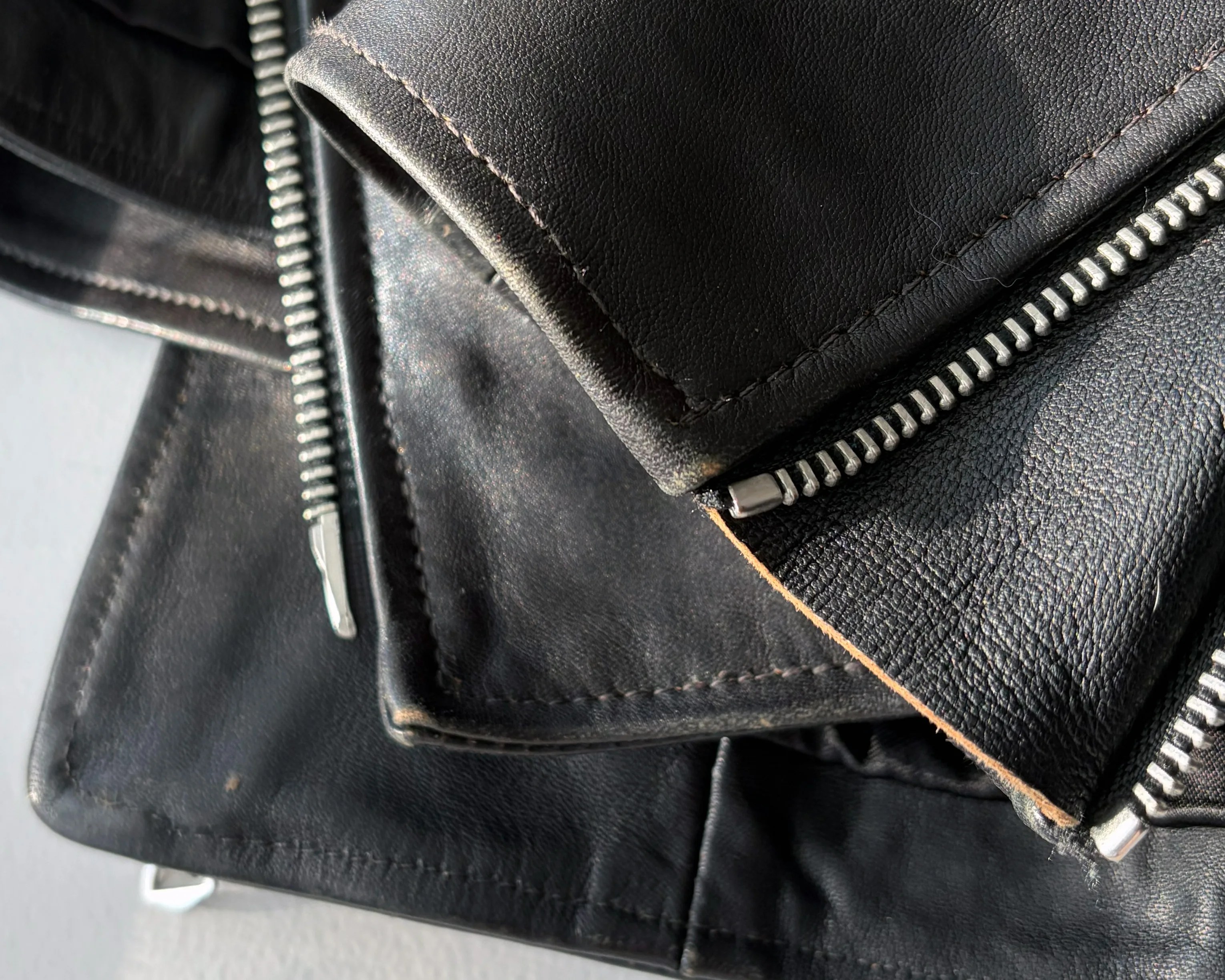 Close-up of black leather jacket with silver zipper and visible stitching.
