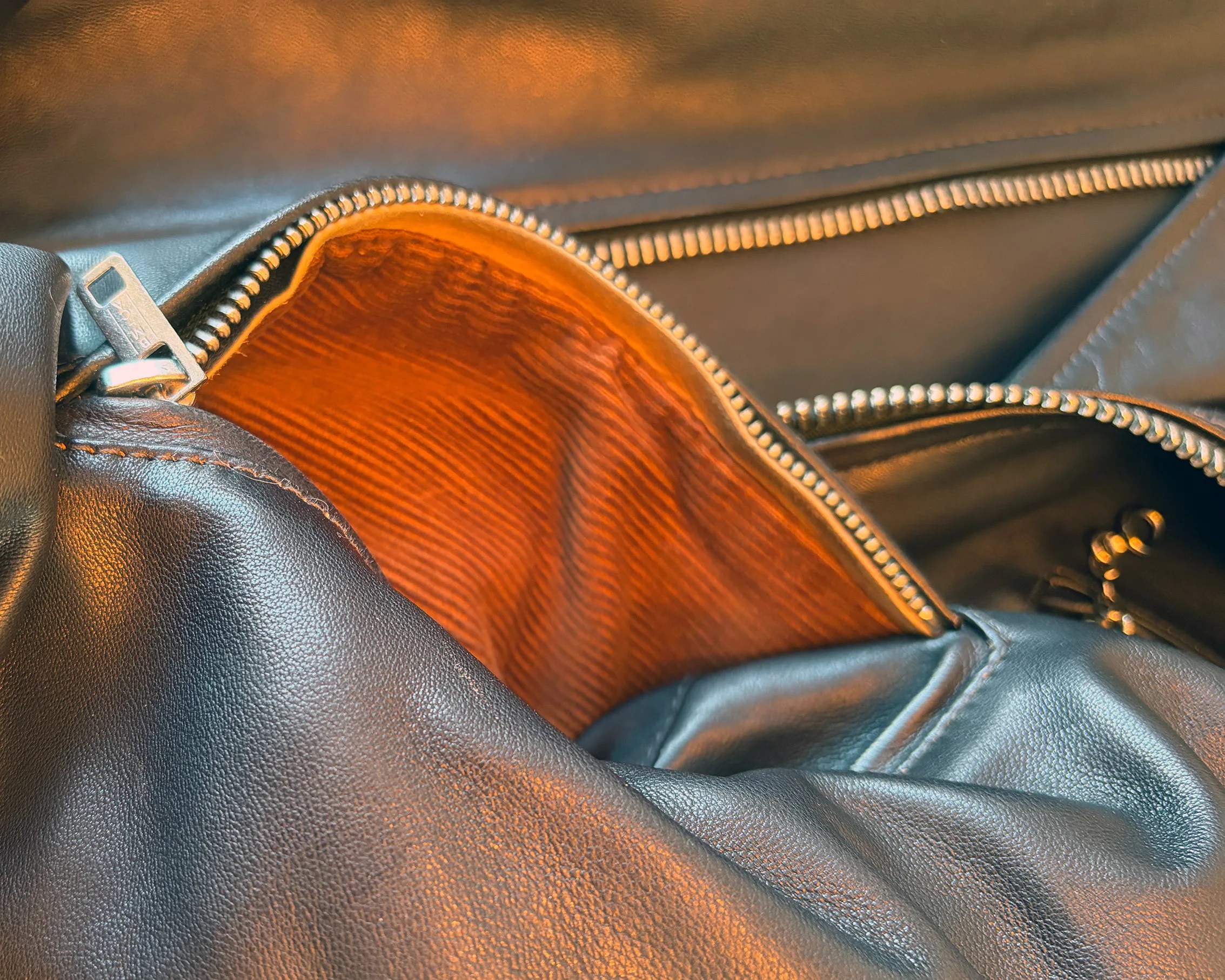 Black leather bag with a partially open zipper revealing an orange fabric interior lining.