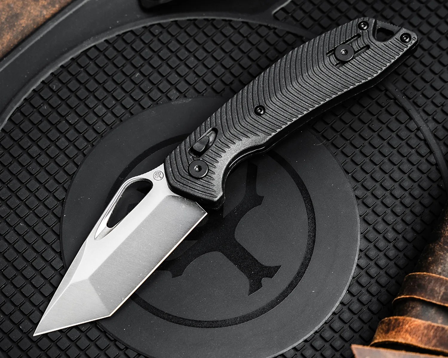 Folding knife with a silver tanto blade and textured black handle on a black rubber mat.
