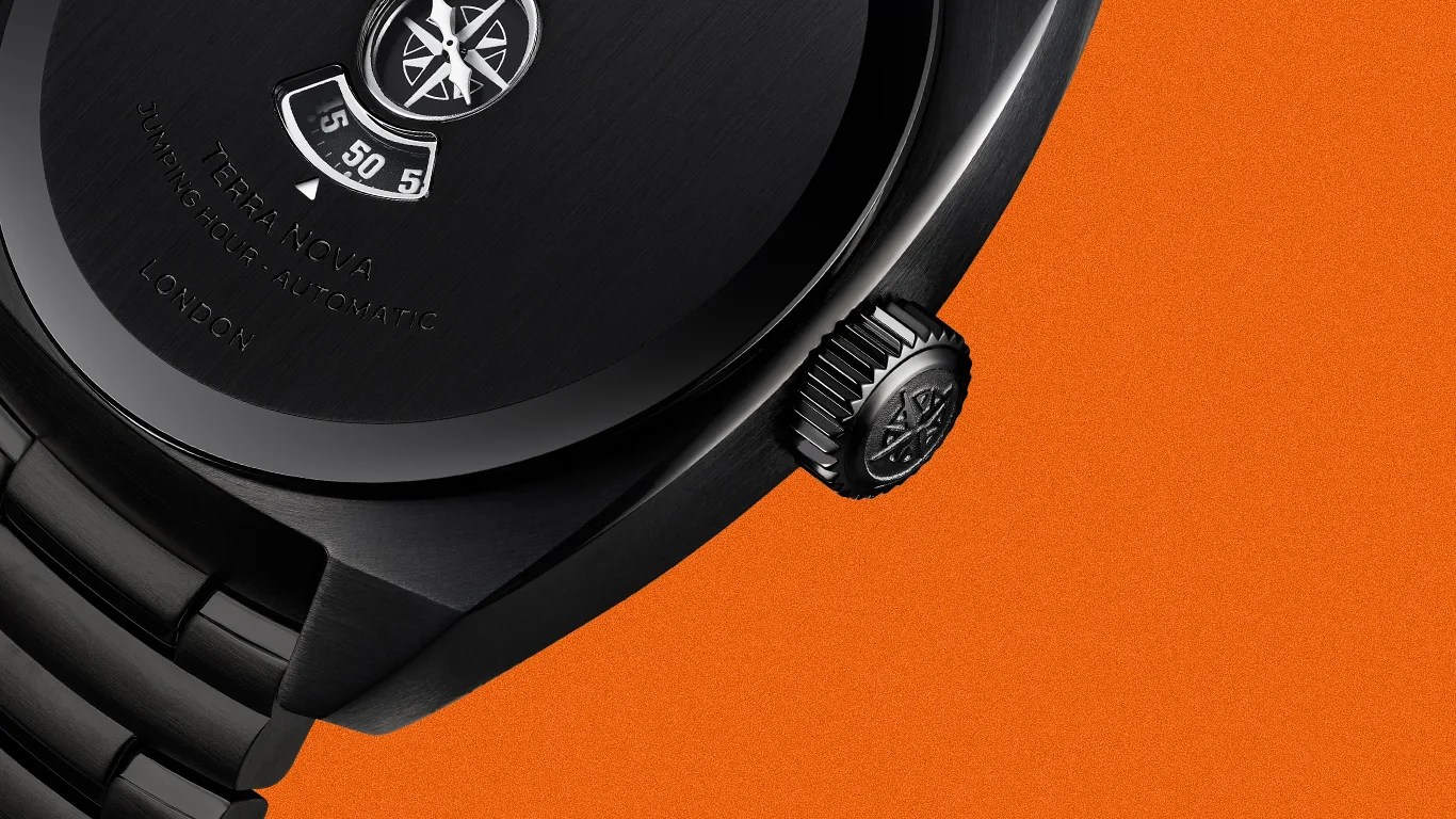 Close-up of a black Terra Nova automatic watch with a compass design on the dial and a black metal bracelet on an orange background.
