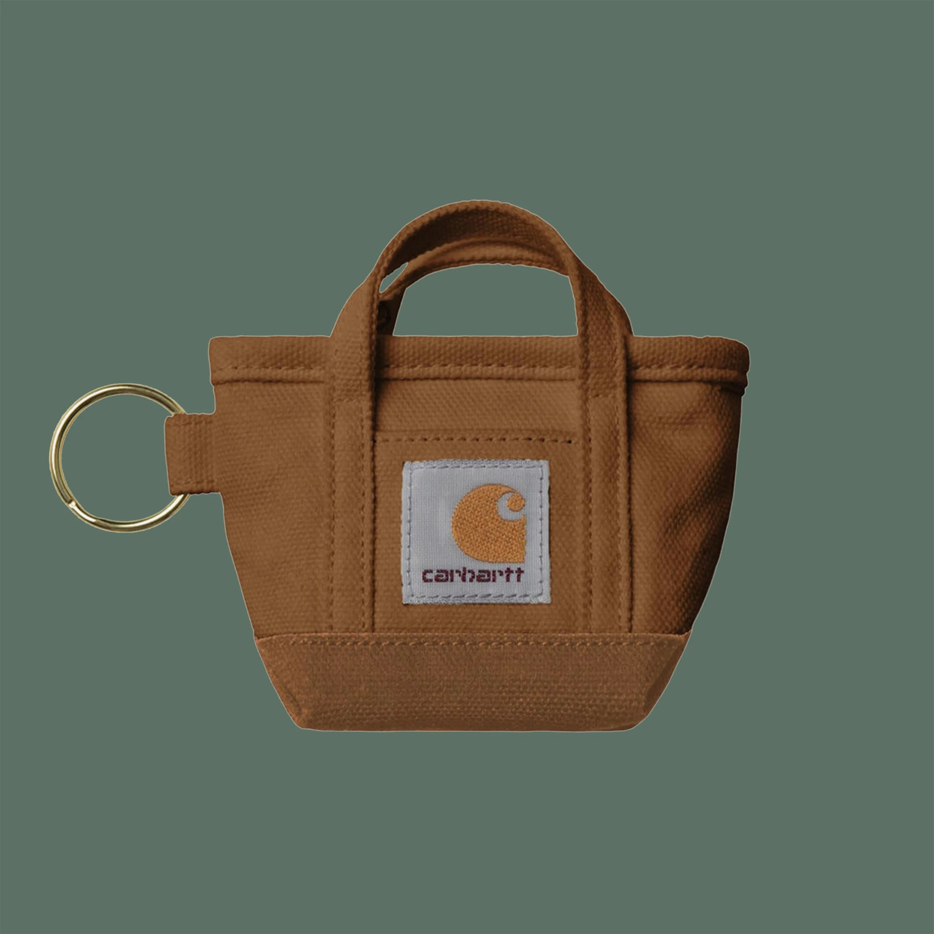 Small brown Carhartt canvas tote bag keychain with a gold metal ring on a green background.