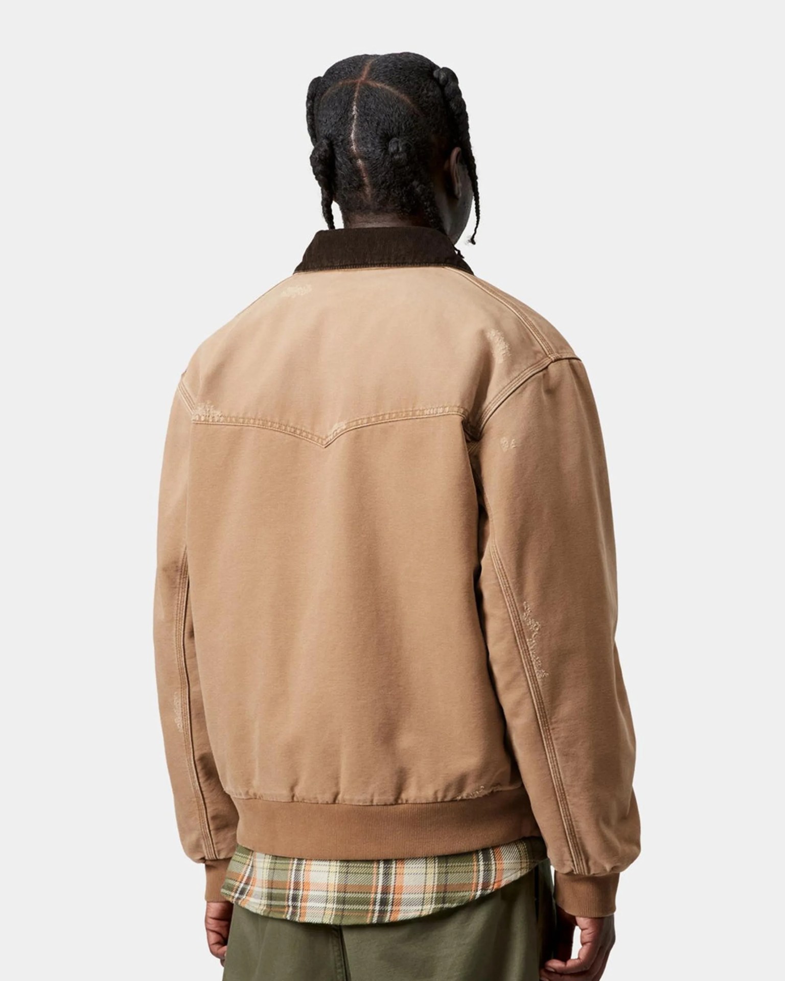 Back view of a person wearing a tan jacket with a dark brown collar over a green and orange plaid shirt.