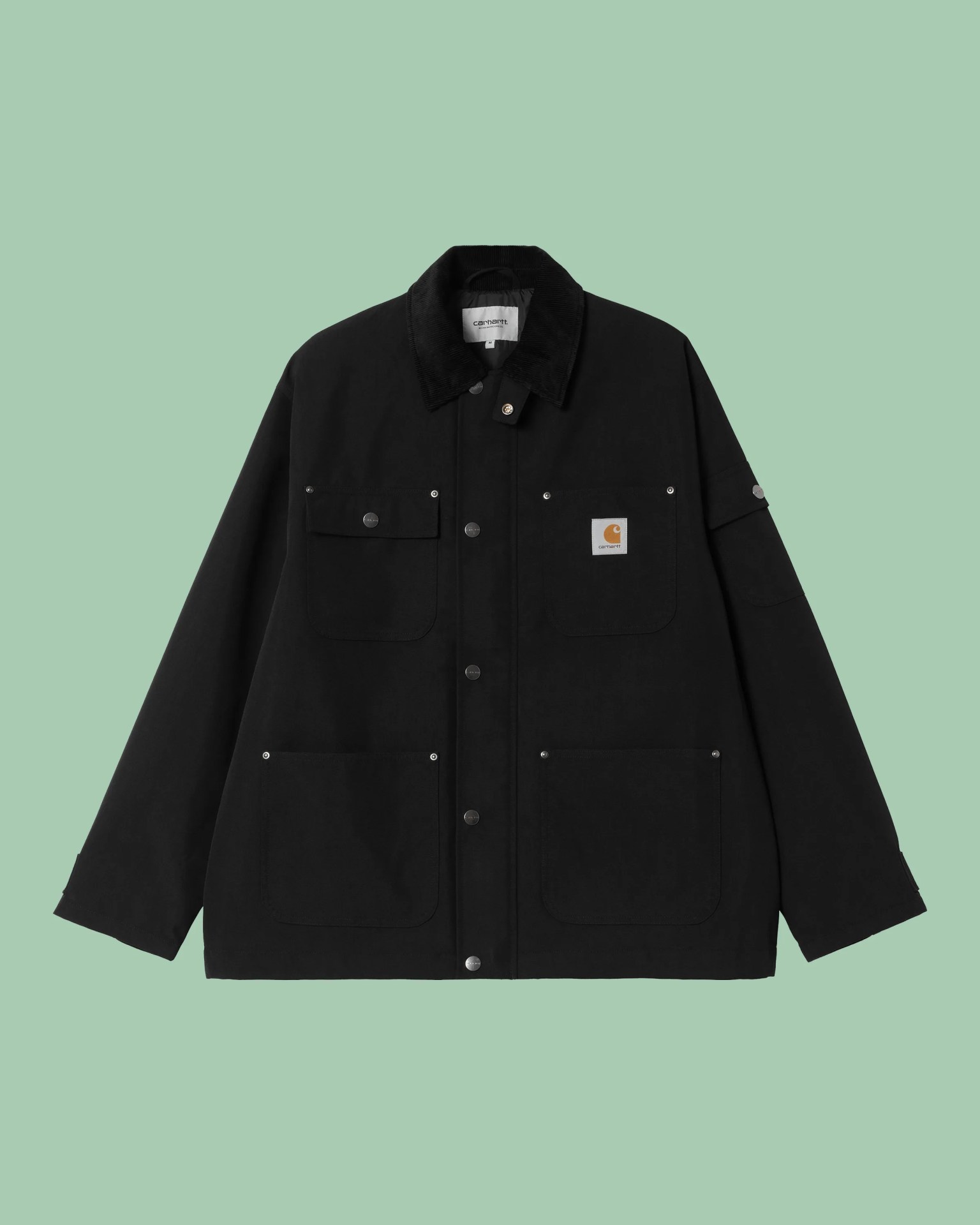 Black Carhartt jacket with snap buttons, four front pockets, and a corduroy collar on a green background.