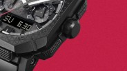Close-up of a black rugged watch with textured bezel and crown against a red background.