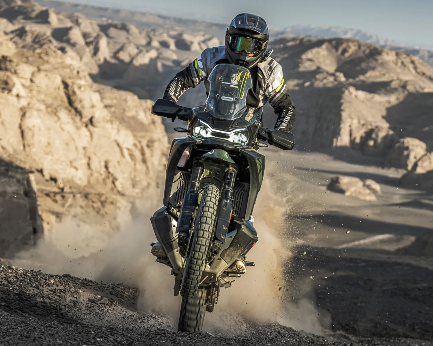 Motorcyclist wearing black and gray gear riding a black off-road motorcycle on a dusty rocky trail.
