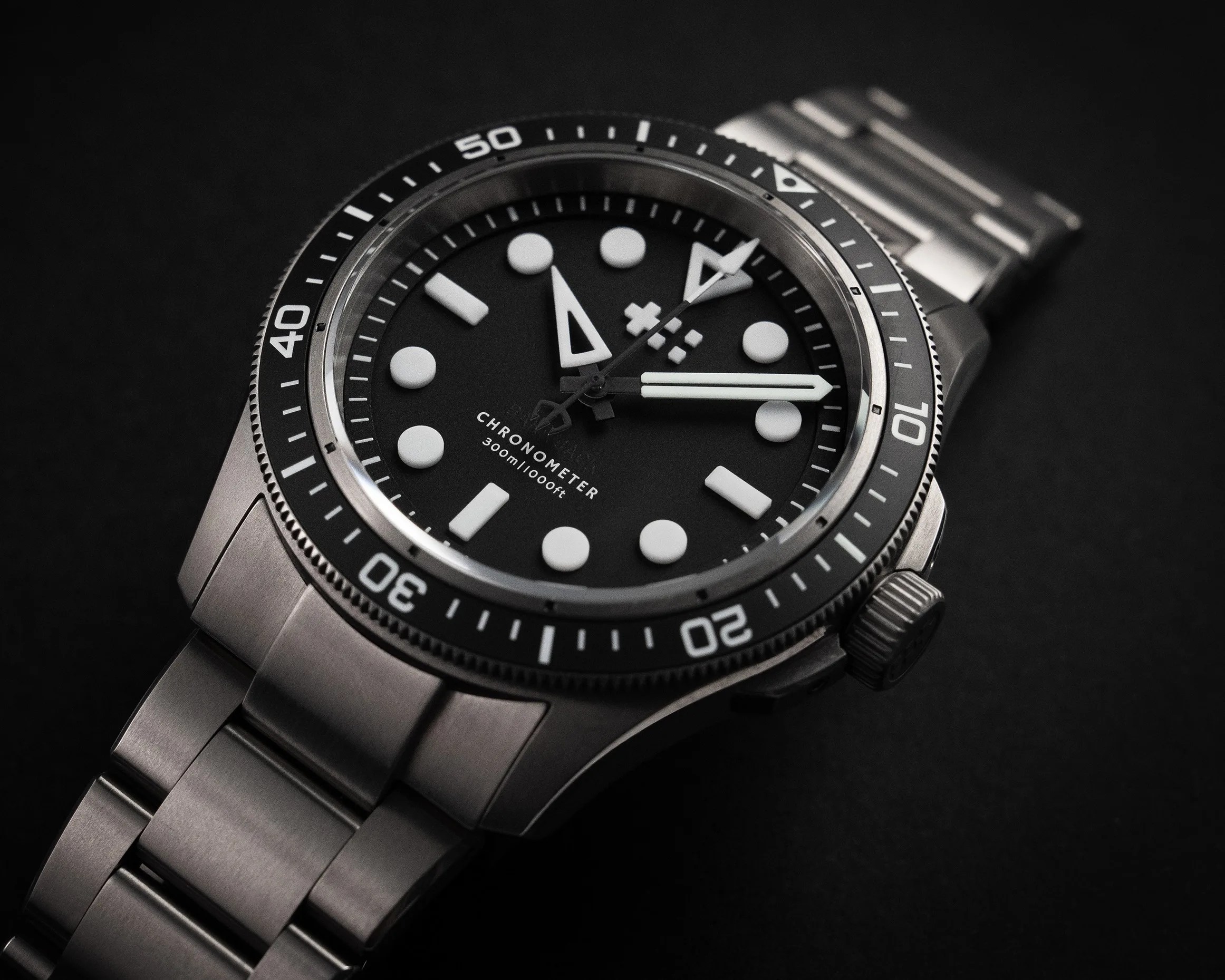 Close-up of a stainless steel dive watch with a black dial, white markers, and a rotating bezel on a black background.