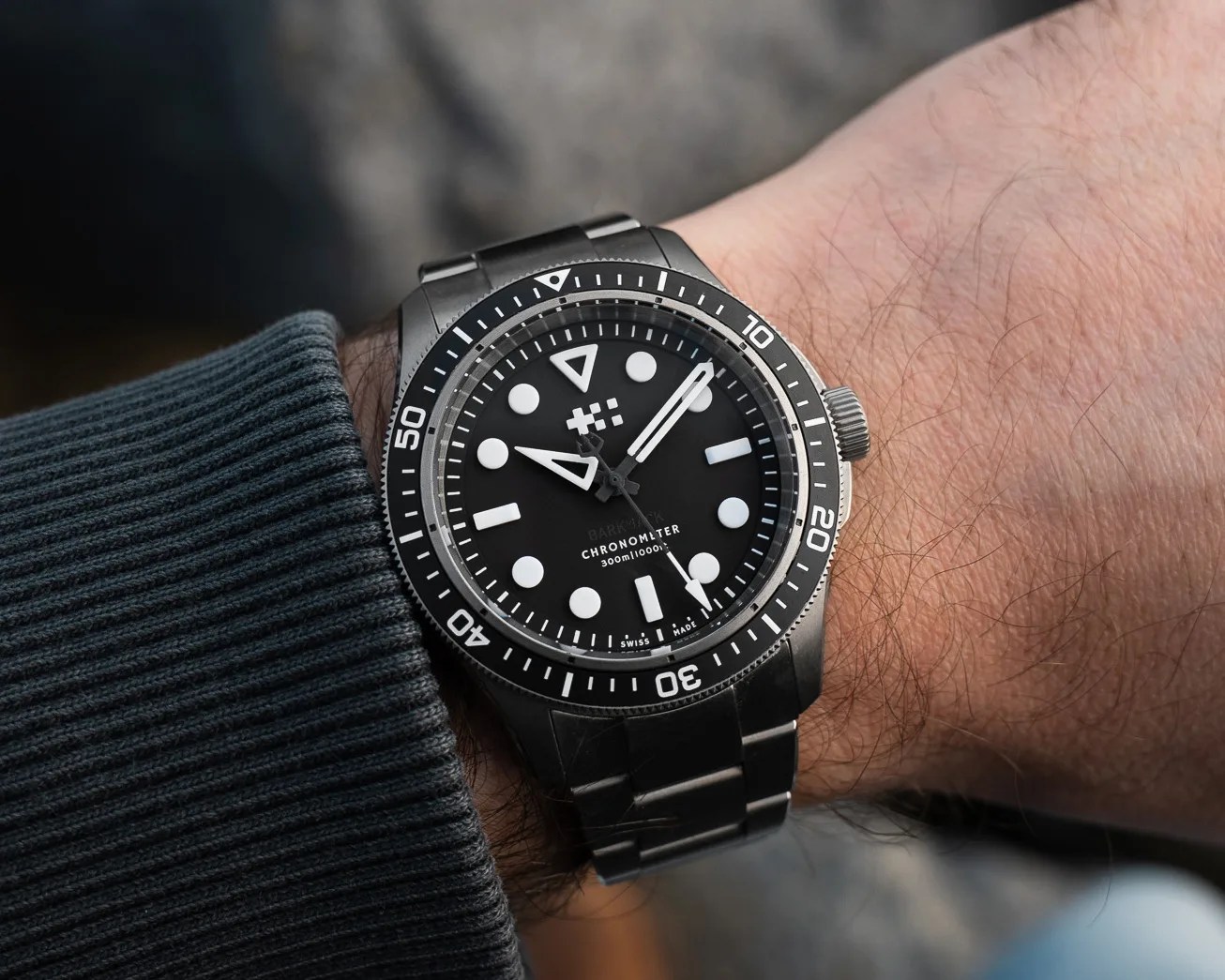 Black dive watch with white markers and a stainless steel bracelet worn on a wrist.