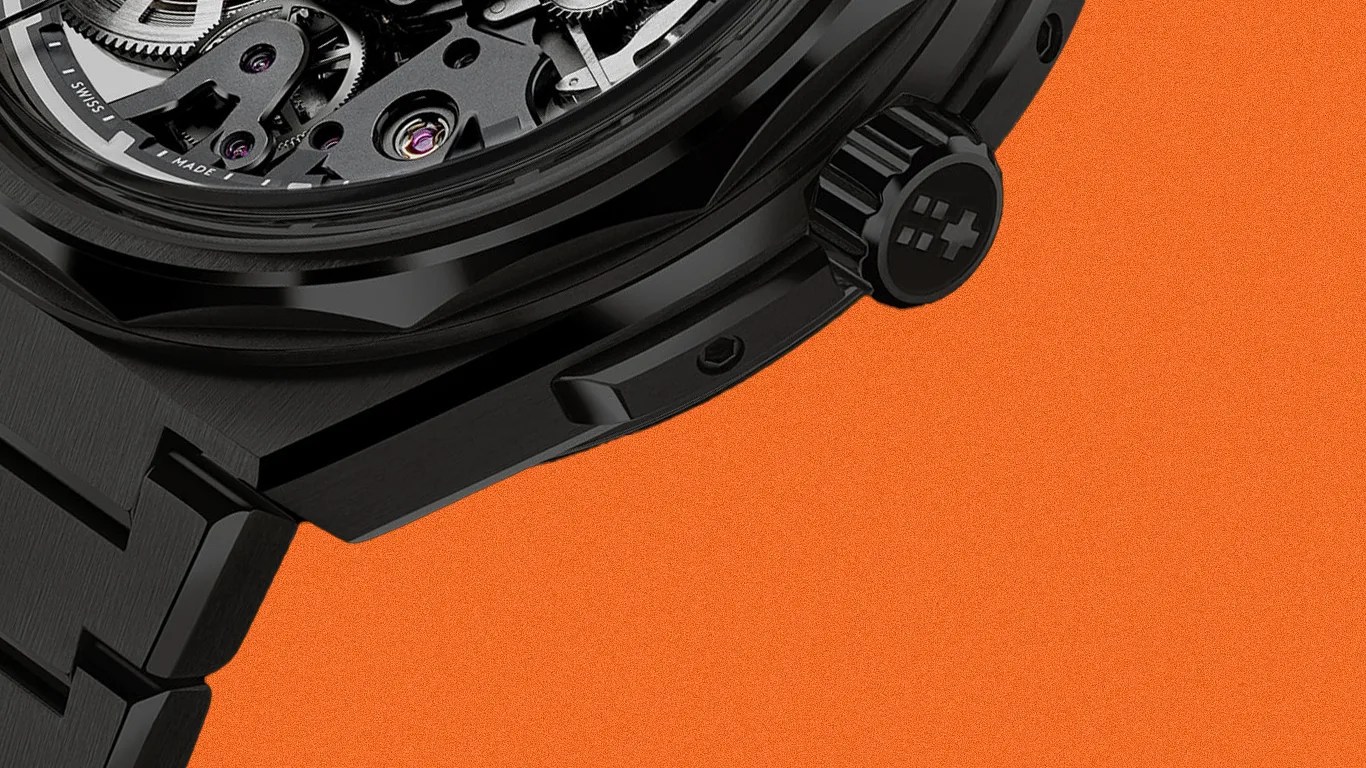 Close-up of a black metal watch crown and part of the bracelet against an orange background.
