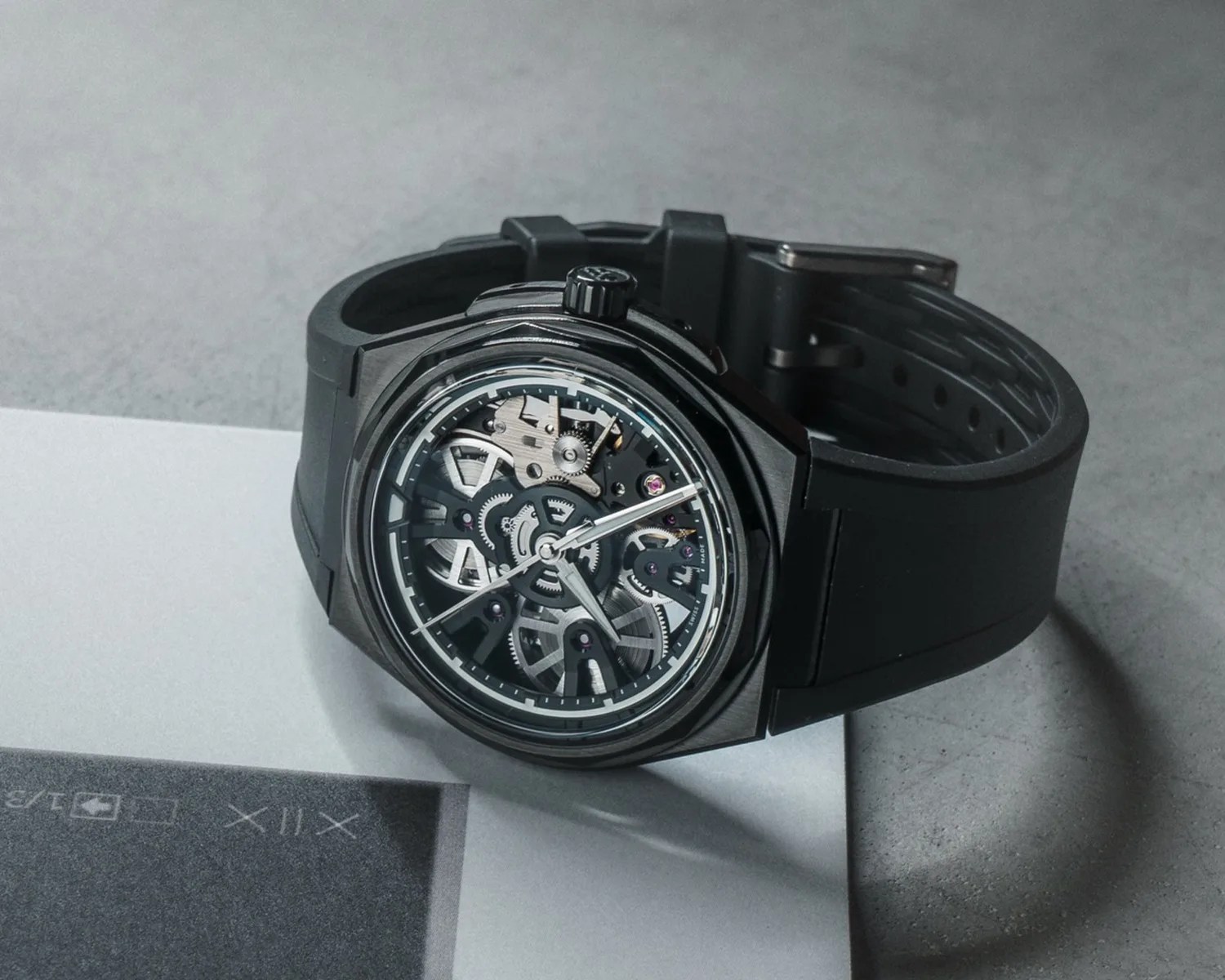 Black wristwatch with a skeleton dial showing internal gears and a black rubber strap on a gray surface.