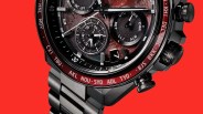 Close-up of a black metal wristwatch with a red bezel showing city abbreviations and multiple subdials on a textured dial.