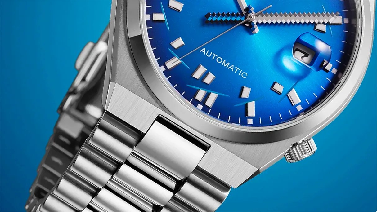 Close-up of a silver metal wristwatch with a blue dial, automatic movement, and date window showing the number 7.