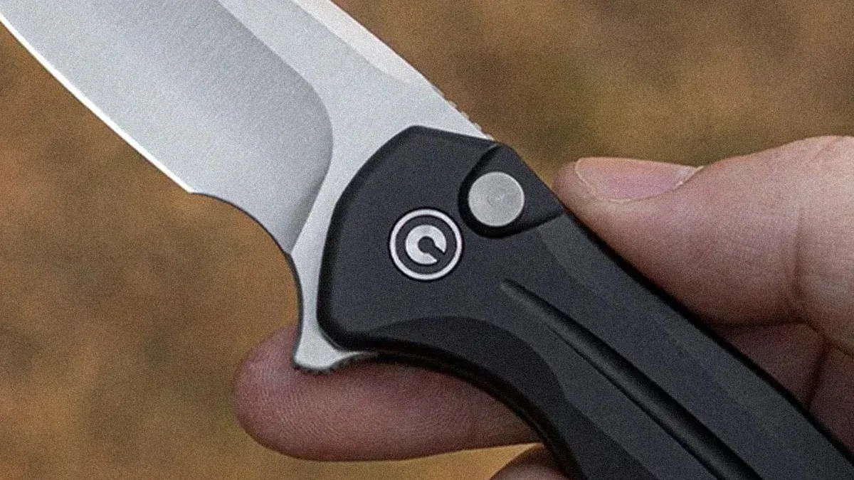 Close-up of a hand holding a folding knife with a silver blade and black handle featuring a circular logo.