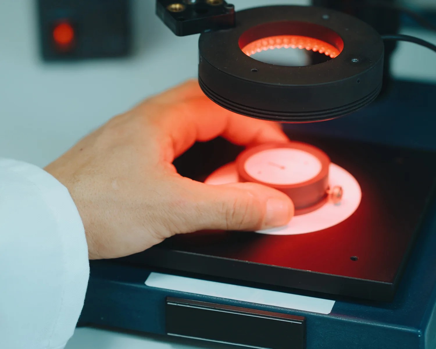 Hand adjusting a round gauge under a circular red light on a black and blue device.