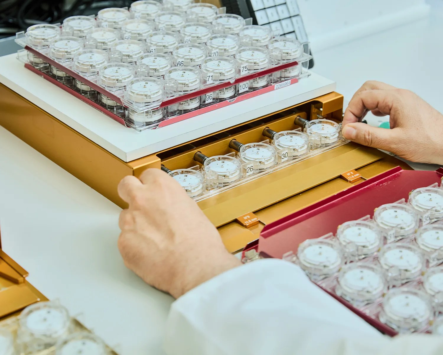 Hands adjusting clear plastic dials with numbered labels on a gold and white laboratory instrument.