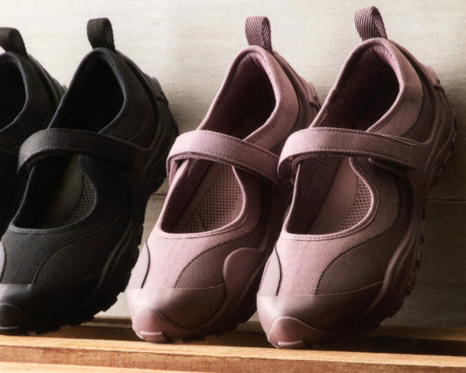 Two pairs of Mary Jane-style shoes with thick soles, one black and one mauve, displayed on a wooden surface.