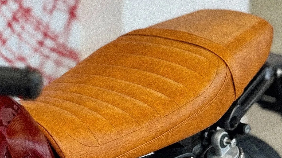 Tan leather motorcycle seat with horizontal stitching on a red bike frame.