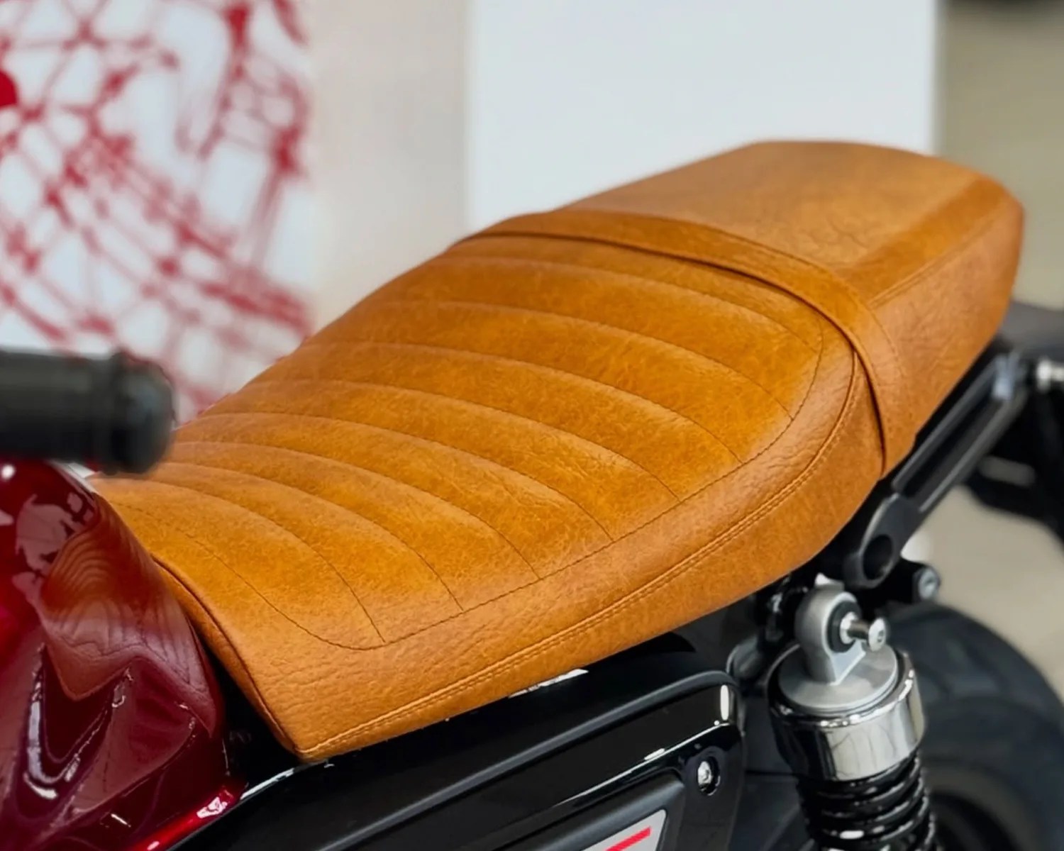 Tan leather motorcycle seat with horizontal stitching on a red and black bike.