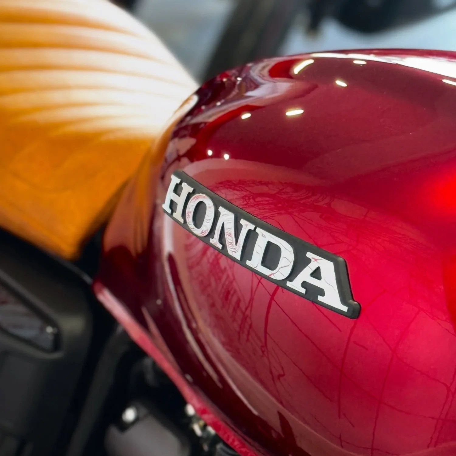 Glossy red Honda motorcycle fuel tank with a tan leather seat in the background.