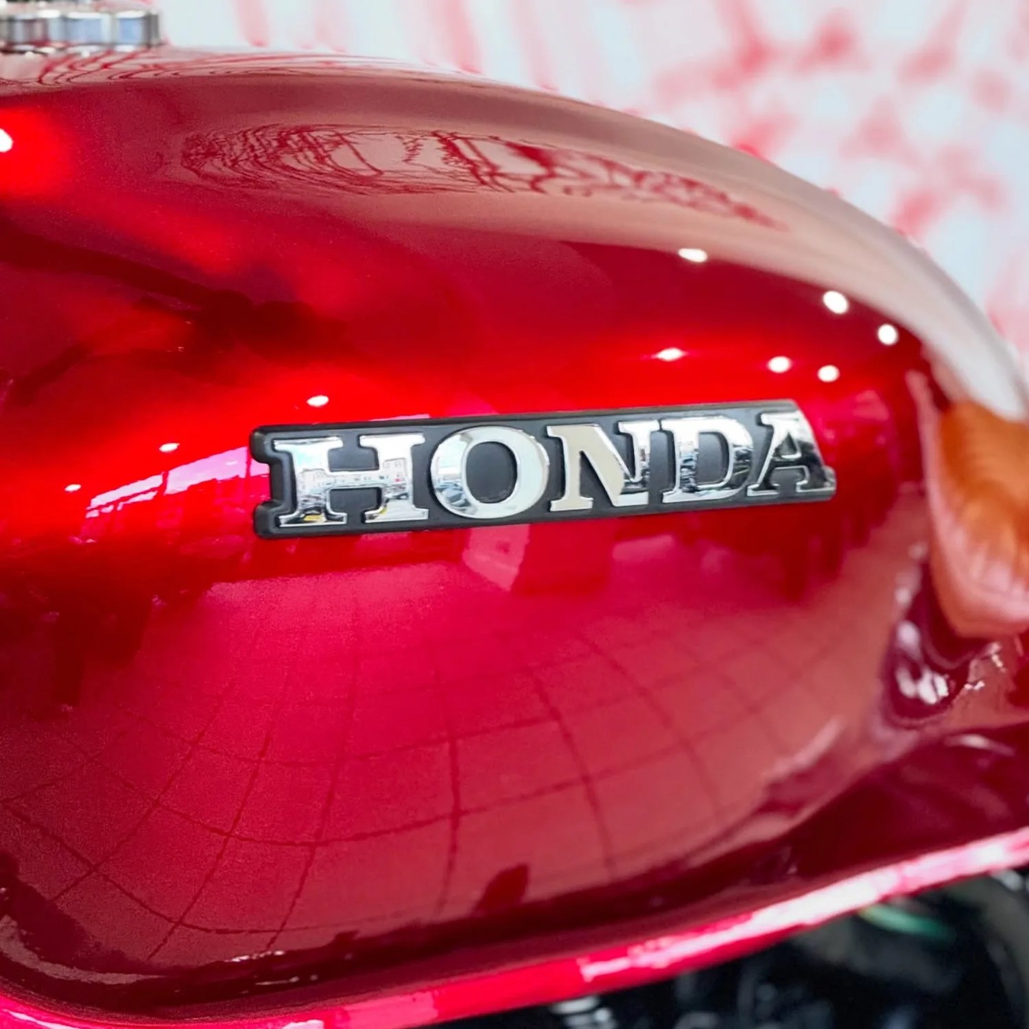 Glossy red motorcycle fuel tank with a silver Honda logo badge.