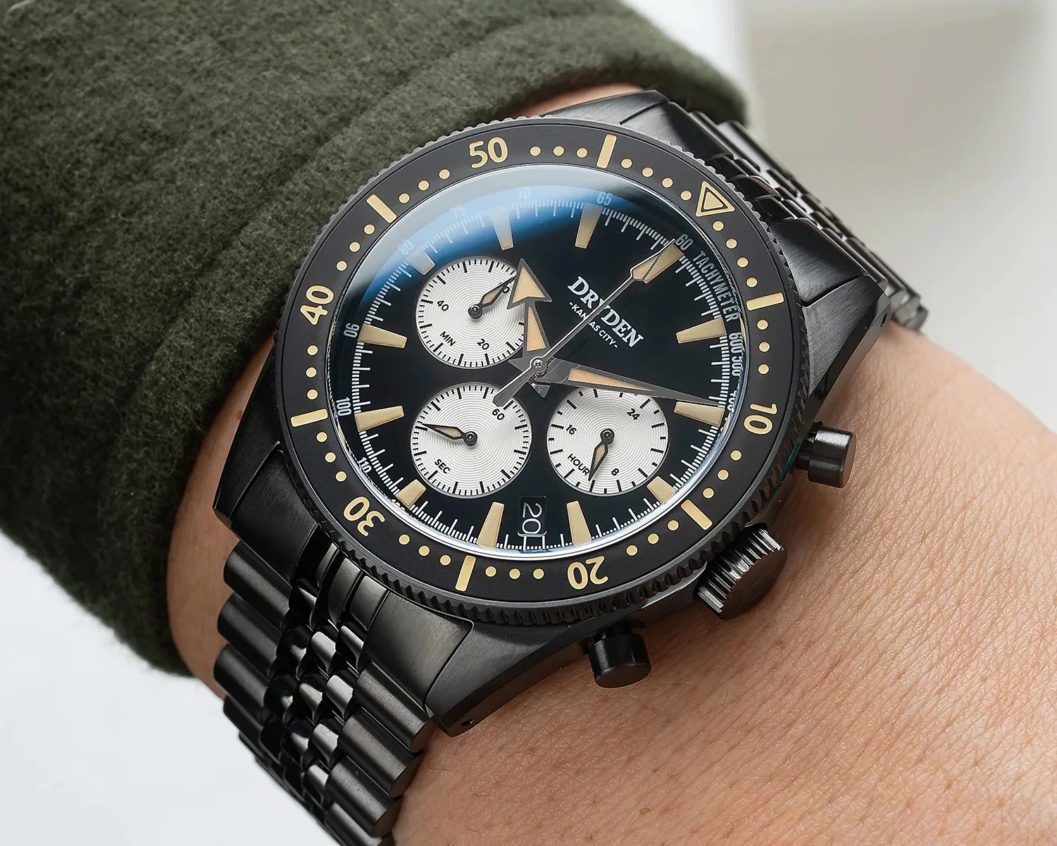 Black metal wristwatch with beige markers, three white subdials, and a tachymeter bezel worn on a wrist.