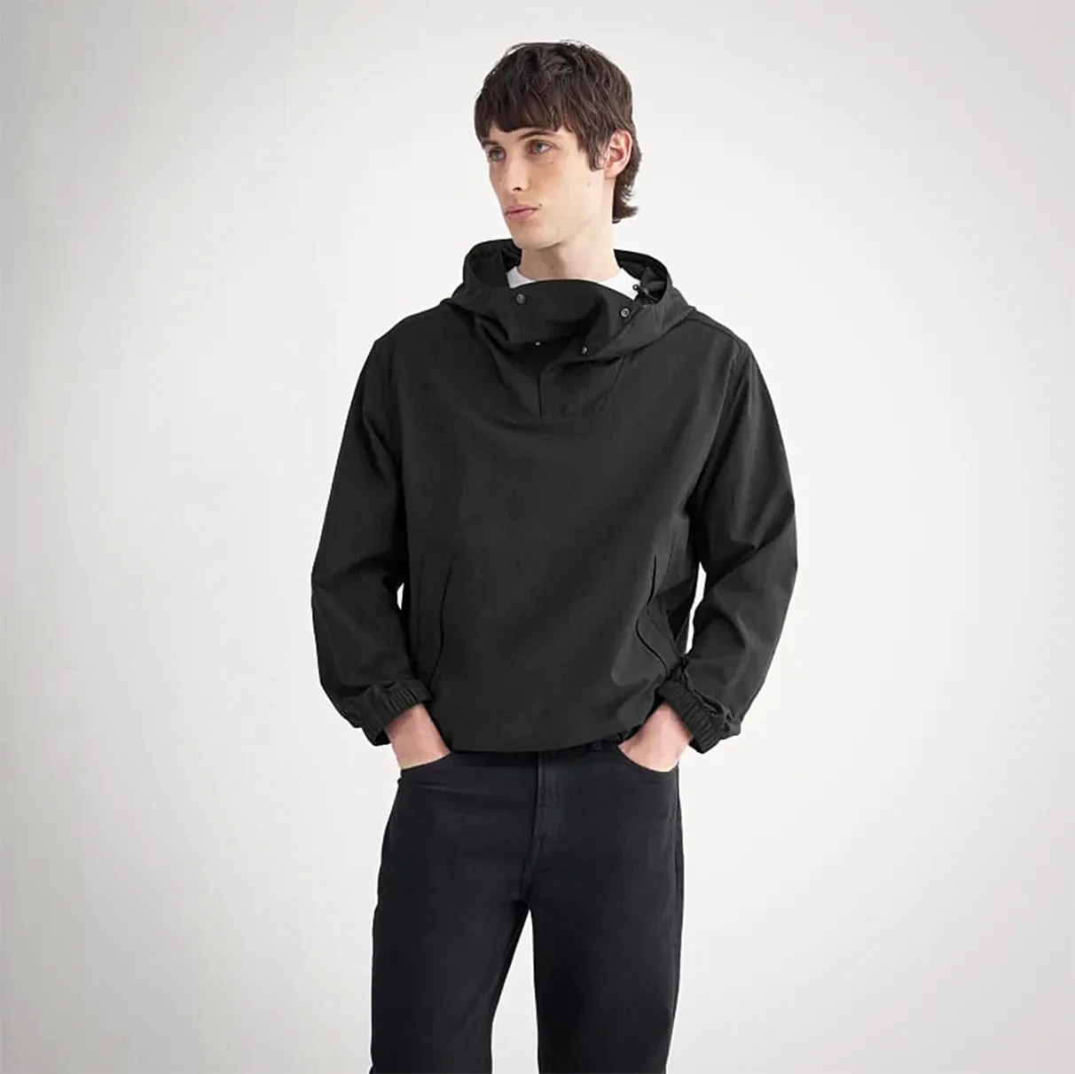 Black hooded pullover jacket with elastic cuffs worn by a person with hands in pockets.