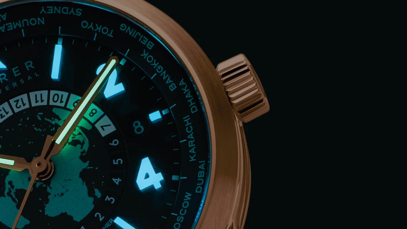 Close-up of a watch face with luminescent hands and hour markers, showing world cities on the bezel.