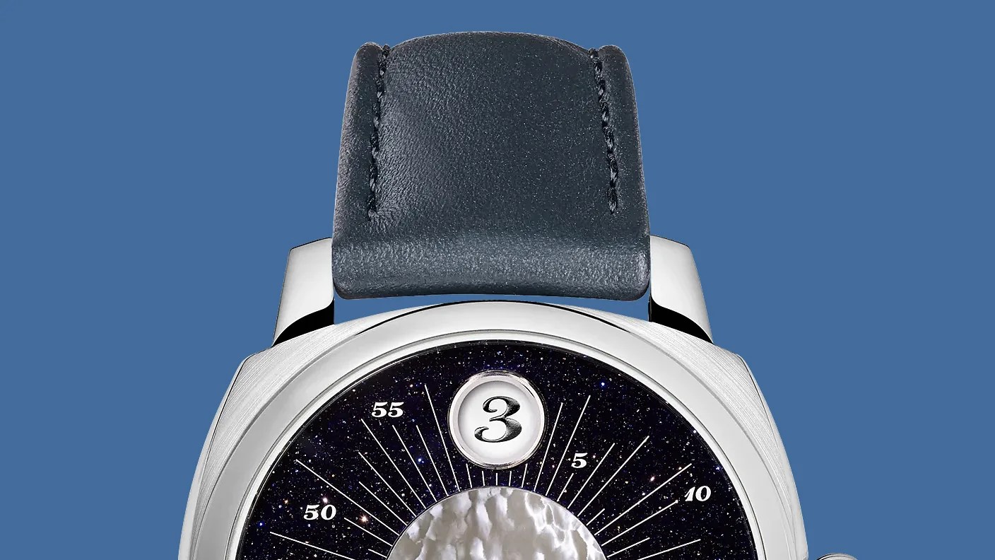 Close-up of a watch with a black leather strap, silver case, and a dark starry dial with a large number 3 at the top.