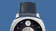 Close-up of a watch with a black leather strap, silver case, and a dark starry dial with a large number 3 at the top.
