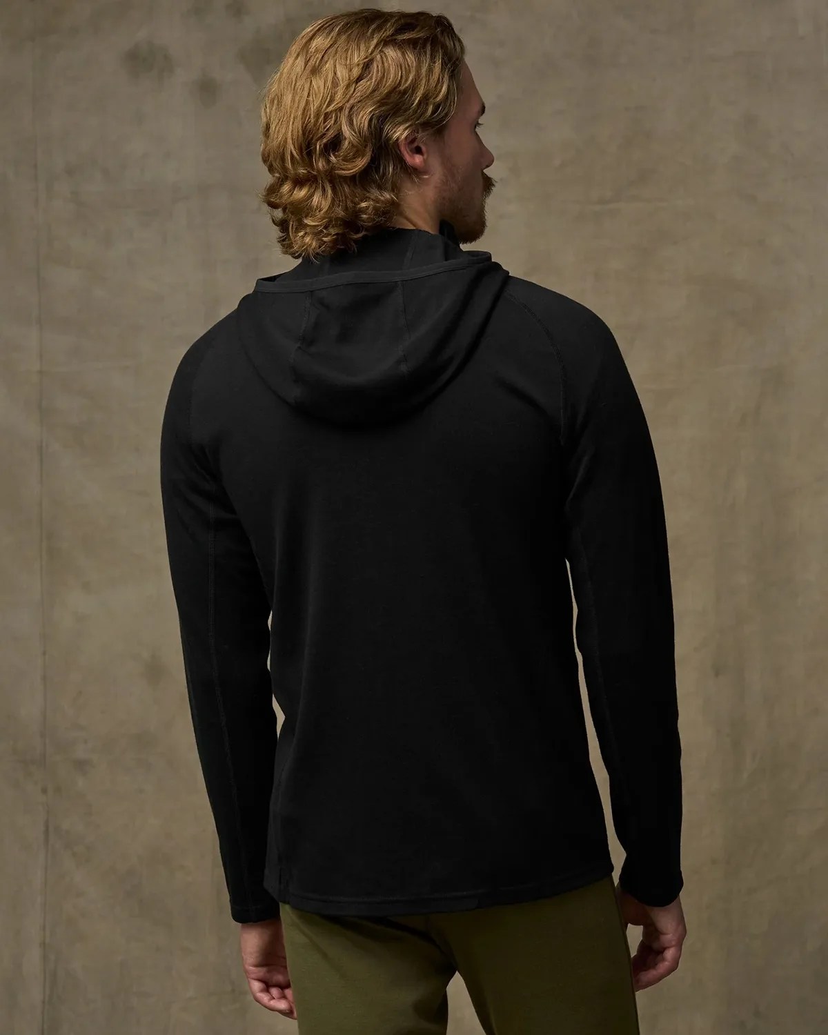 Black long-sleeve hooded shirt worn by a person facing away against a plain brown background.